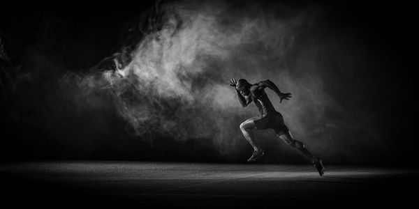 Athlète sprinter courant dans la fumée en noir et blanc.