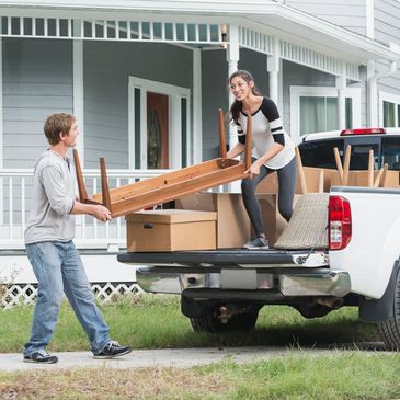 Couple unloading furniture from a truck in front of their house.