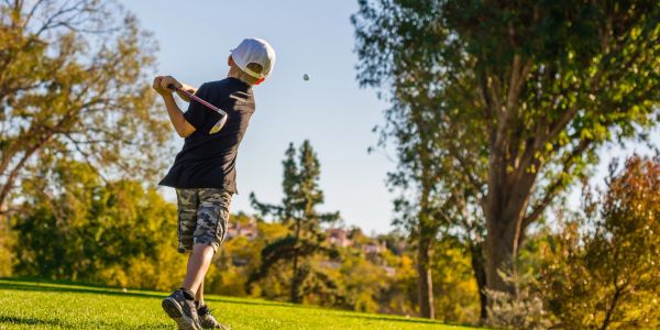 Young boy hitting a golf ball on a sunny course.