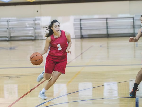 Female basketball player in red dribbling the ball on court.