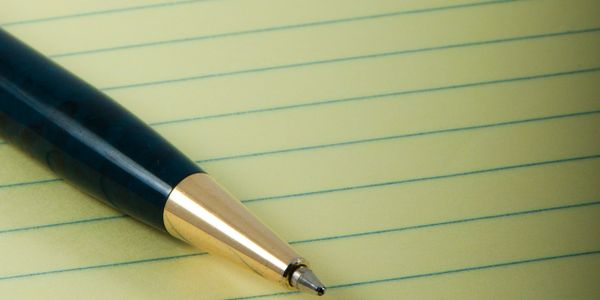 A ballpoint pen resting on a yellow lined notebook.