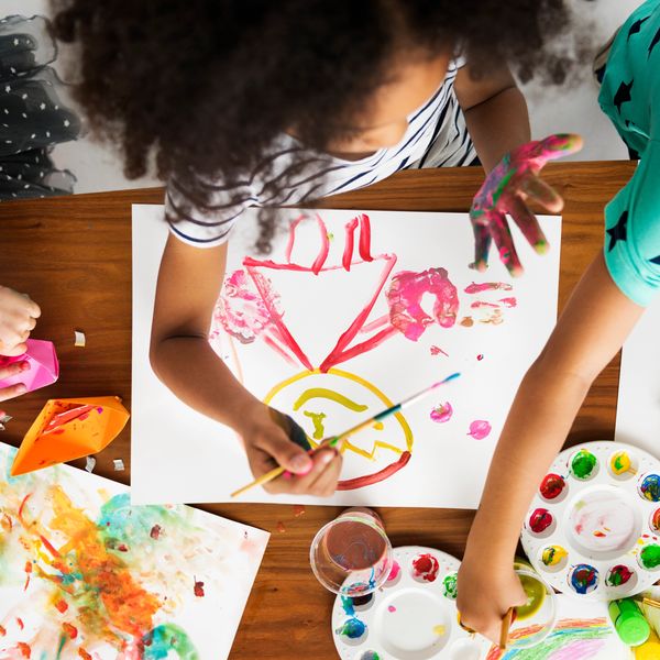 Children painting colorful pictures with brushes and hands at a table.