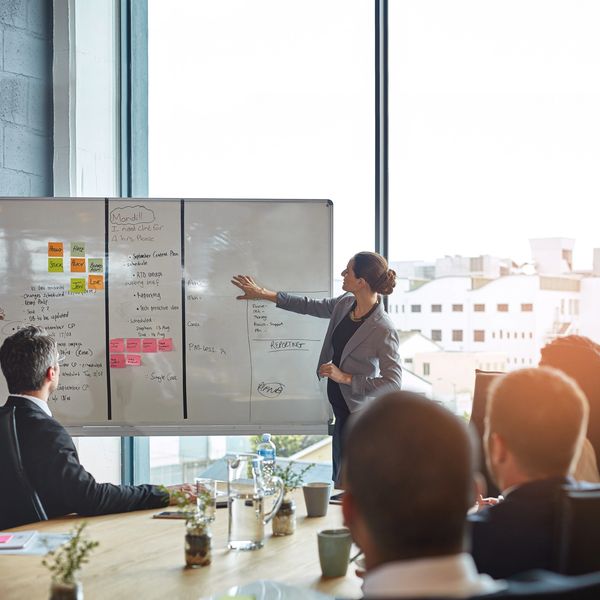 Businesswoman presenting ideas on a whiteboard to colleagues in a modern office.