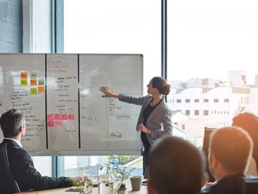 A woman presents ideas on a whiteboard to colleagues in a modern office.
