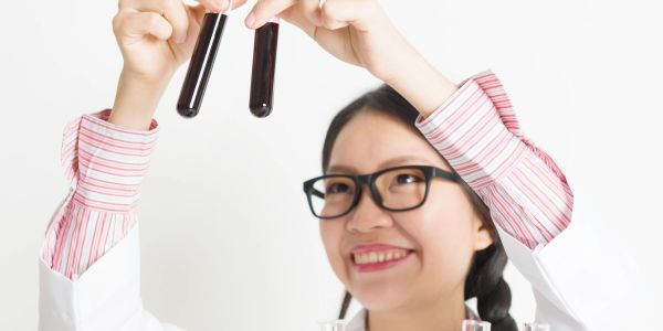 Scientist examining two test tubes with dark liquid in a lab.