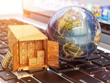 A globe and shipping container with boxes on a keyboard symbolizing global e-commerce.