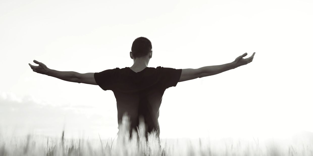 Person standing with arms wide open in a field.