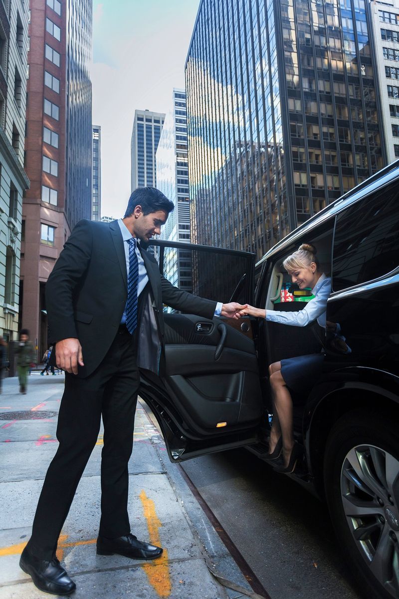 Young male driver helping a happy female passanger getting our of luxury black car in New York City