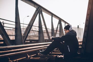 A man sitting on train tracks wearing headphones and a beanie.