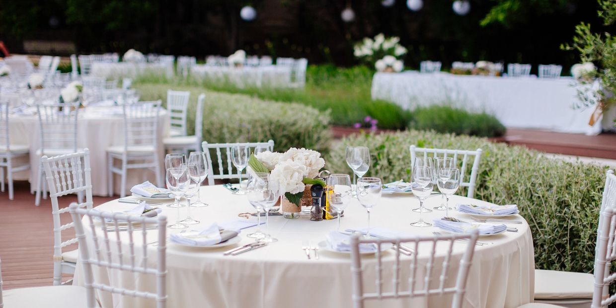 Elegant outdoor banquet tables set with white linens and floral centerpieces.
