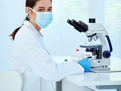Scientist in lab coat and mask using a microscope in a laboratory.