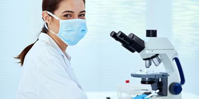 Scientist wearing a mask working with a microscope in a lab.