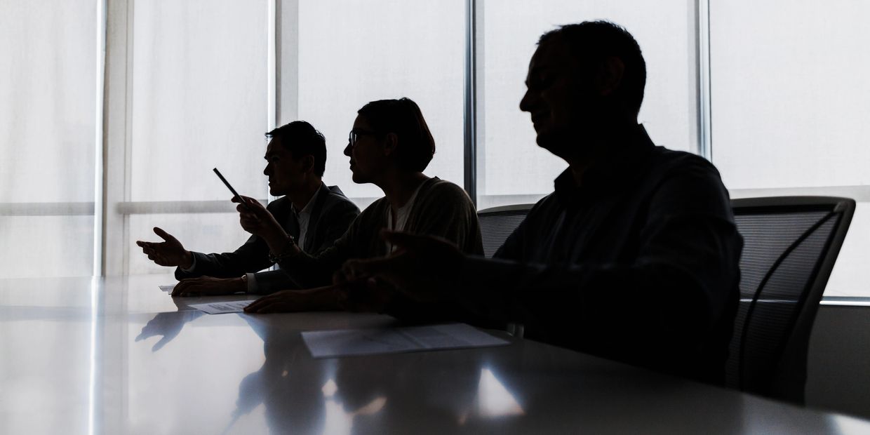 Silhouettes of three people in a meeting room.