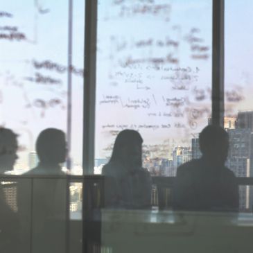 Silhouettes of four people in a meeting room with glass wall covered in handwritten notes.