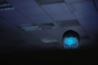 Man illuminated by blue light behind a screen.