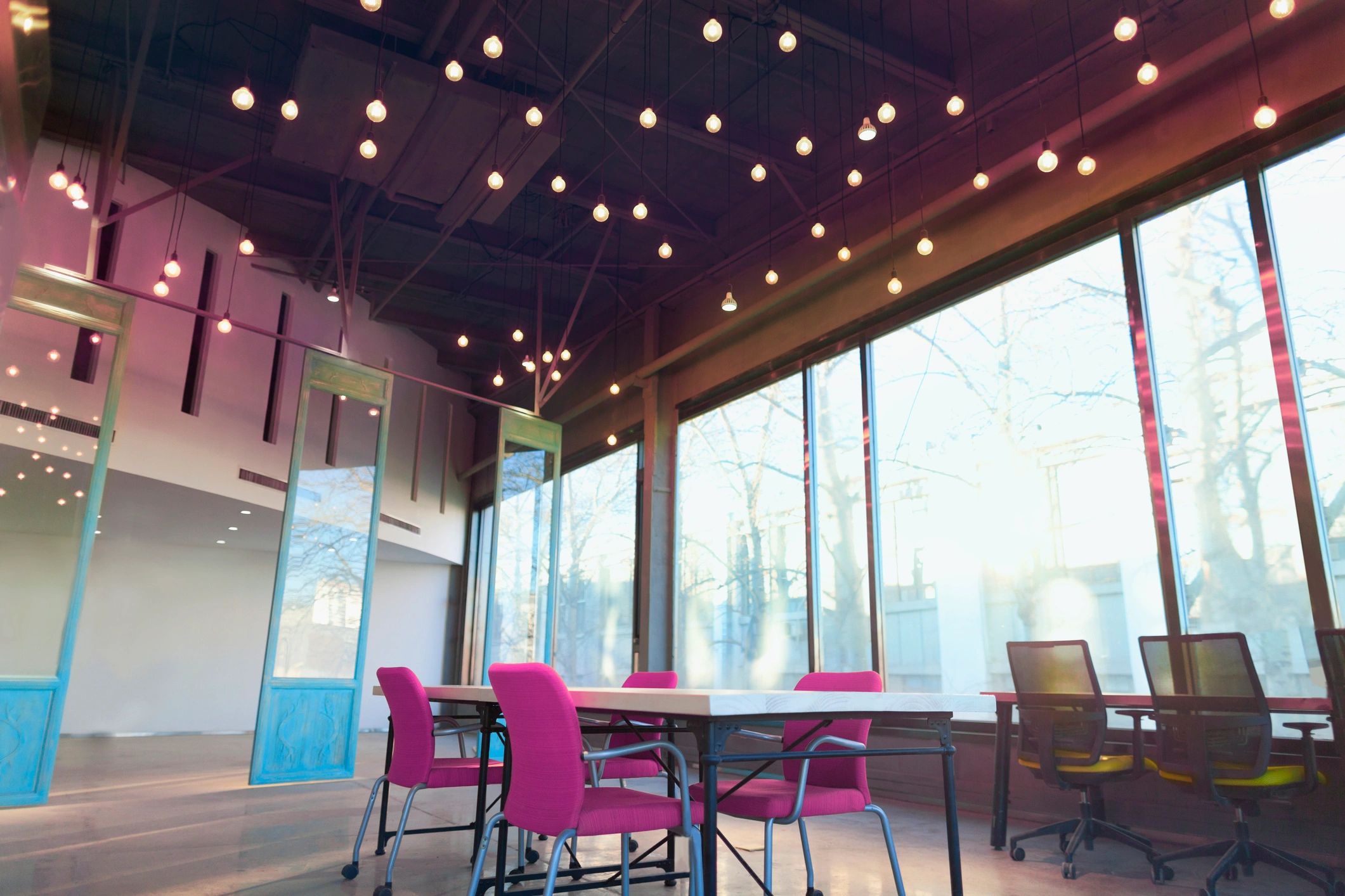 Modern office space with bright pink chairs and hanging light bulbs.