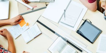 People collaborating with books, notebooks, and a tablet on a table.