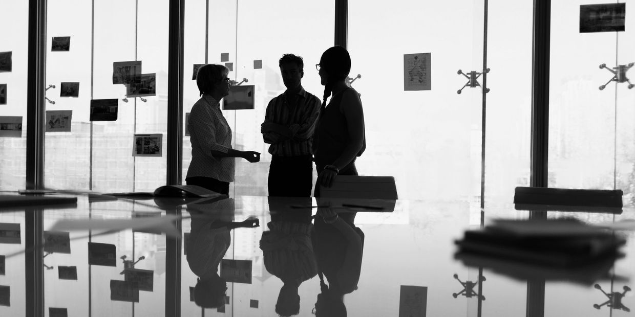 Silhouetted group meeting in office with reflection on table.