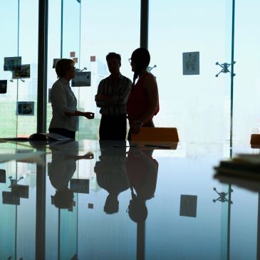 Three people talking in an office with reflections visible on the table.