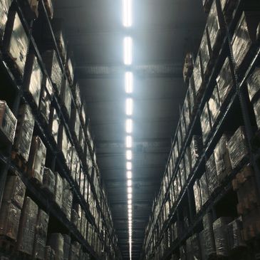 A warehouse aisle with tall shelves filled with stacked boxes under bright lights.