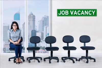 Woman sitting waiting for a job interview with empty chairs and job vacancy sign.
