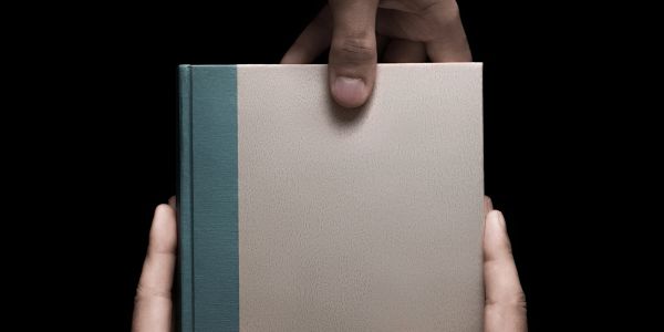 Two hands holding a blank book against a black background.
