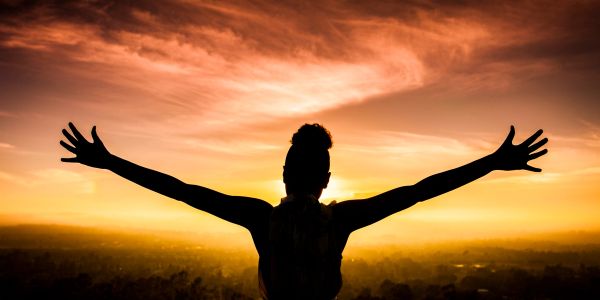 Silhouette of a person with arms outstretched against a vibrant sunset.