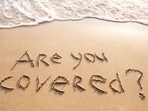 Message 'Are you covered?' written on the sand at the beach.