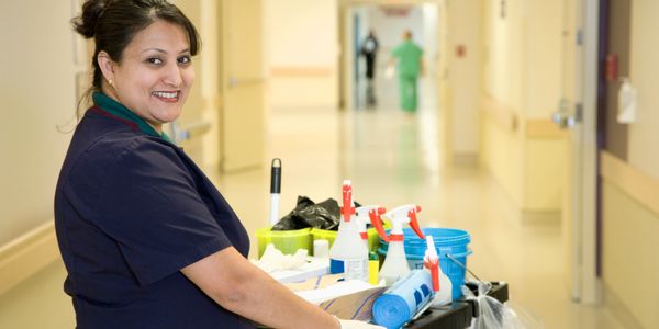 Smiling janitor with cleaning supplies in a hospital hallway.