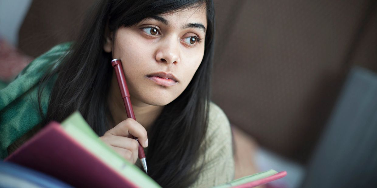 Young woman thoughtfully studying with a pen and notebook.