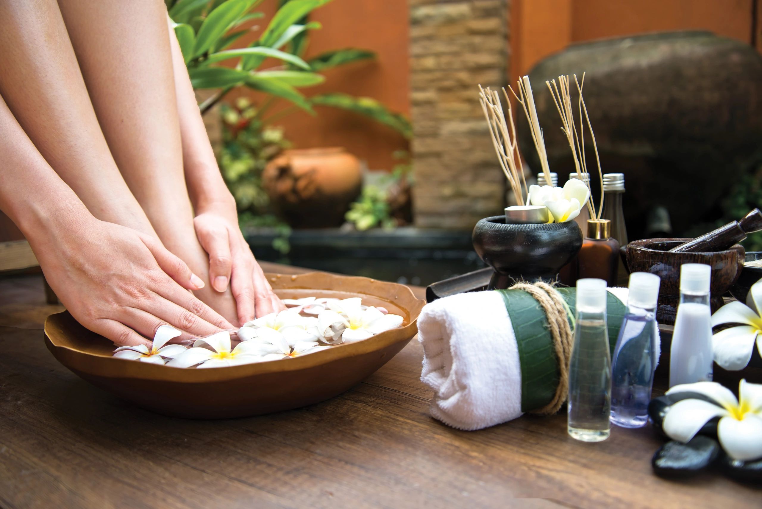Hands soaking in a floral foot bath with spa essentials nearby.