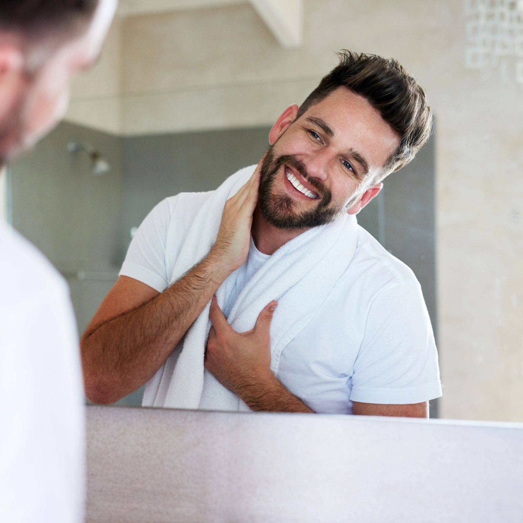 Smiling man with a towel around his neck looking in the mirror.