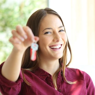 Smiling woman holding a key with a red keychain, symbolizing new home or success.