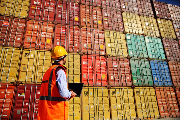 Worker in safety gear communicating at a busy cargo shipping yard.