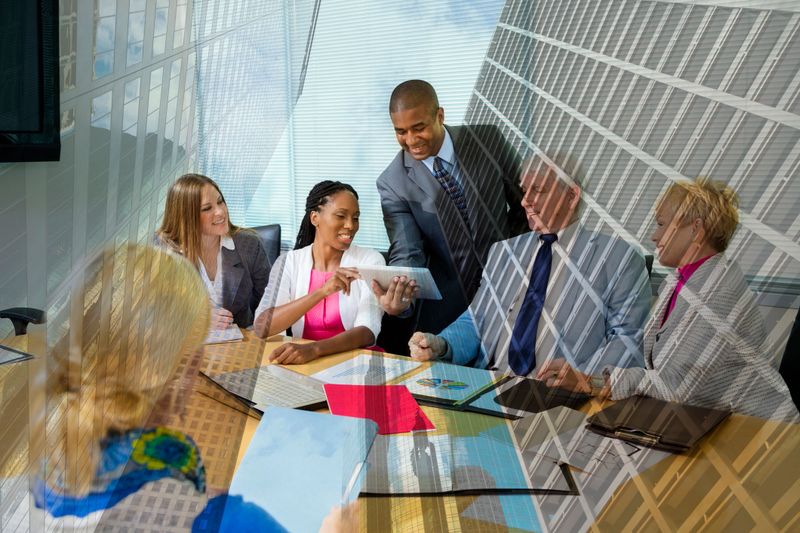 Diverse group of business professionals share data results during an office meeting overlayed onto an image of downtown Houston, Texas, USA skyscraper buildings.