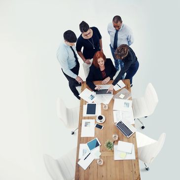Five professionals collaborating around a table with laptops and documents.