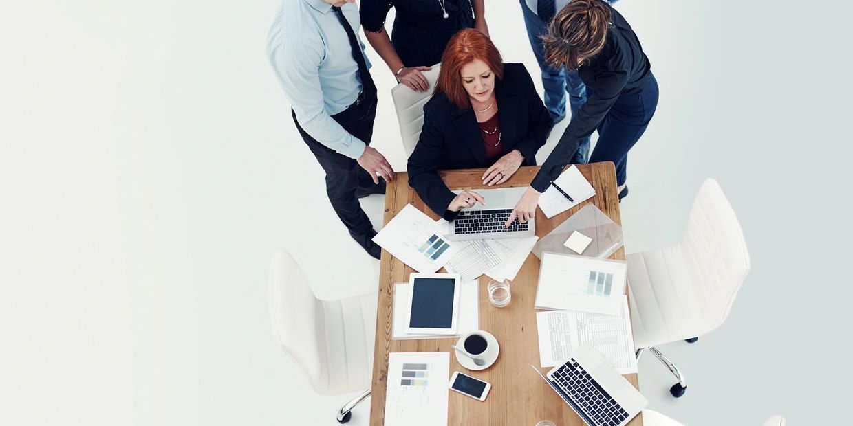 A group of professionals collaborating around a table with laptops and documents.