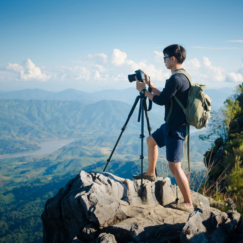 Young traveler standing on big cliff in the mountains and looks into the distance at sunset.