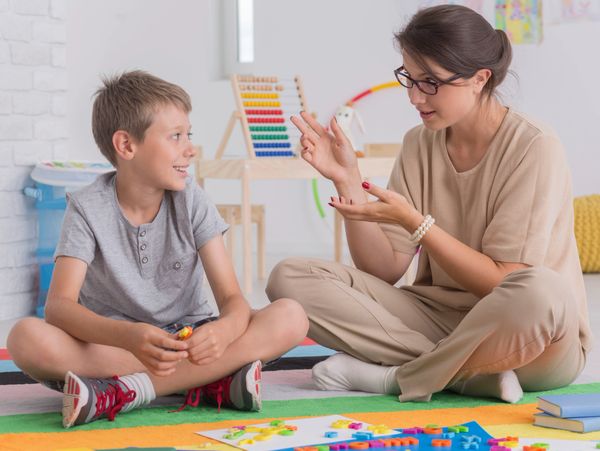 A woman teaching a boy sitting on a colorful carpet with educational toys.