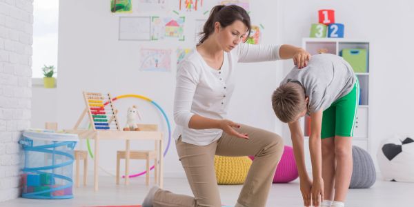 Woman helping boy stretch by touching his back.