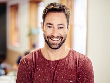 Smiling man in a red shirt with arms crossed indoors.