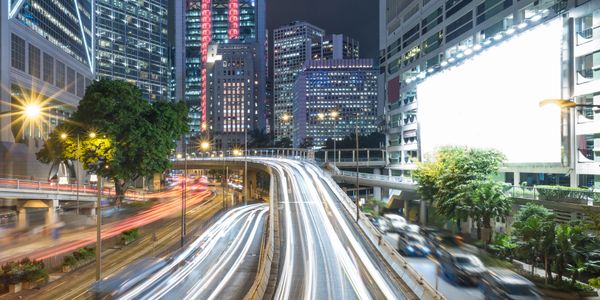 Light trails on a busy urban highway at night with city skyscrapers in the background.