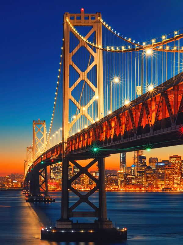 San Francisco Bay Bridge at sunset with city lights, showcasing major venues for corporate events.