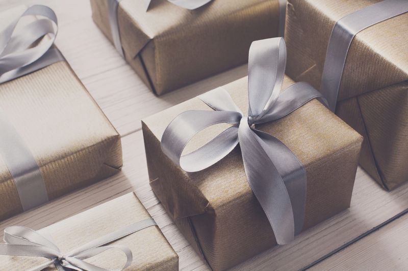 Gift boxes on white wood background. Presents in gold paper decorated with stylish elegant silver satin ribbon bows. Christmas and any other holidays concept