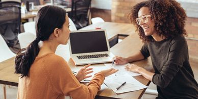 Two women discussing work with a laptop and documents.