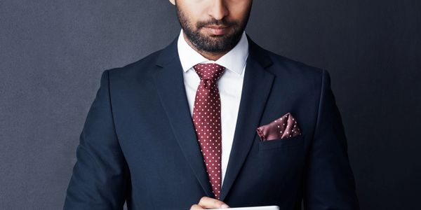 Man in navy blue suit with polka dot tie and pocket square using a tablet.
