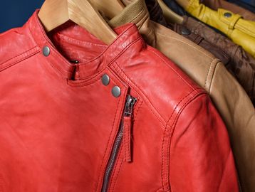 Close-up of colorful leather jackets hanging on wooden hangers.