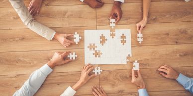 Hands collaborating on assembling a puzzle on a wooden table.