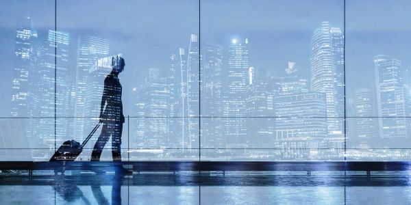Silhouette of a traveler with luggage against a city skyline at night.
