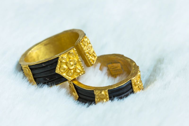 Couple rings are made of gold, and carved floral motifs on both ends. The carved sections are in unsharpened edges. Both ends of the rings are left open for size adjustments. The couple rings are placed on soft white wool.